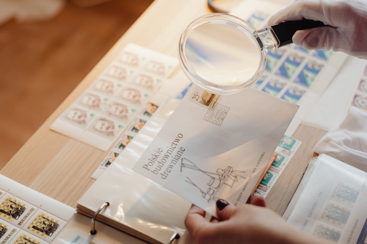 services-03 Gloved hands hold a magnifying glass over postage stamps on white paper with a wooden background.