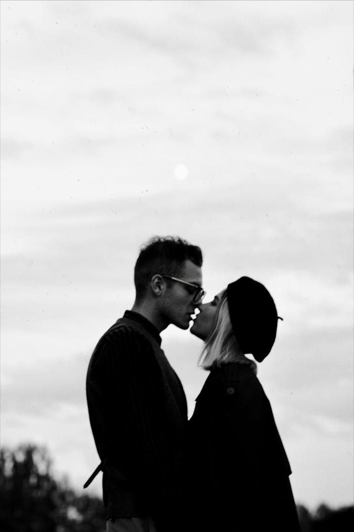 A romantic black and white silhouette of a couple kissing outdoors.
