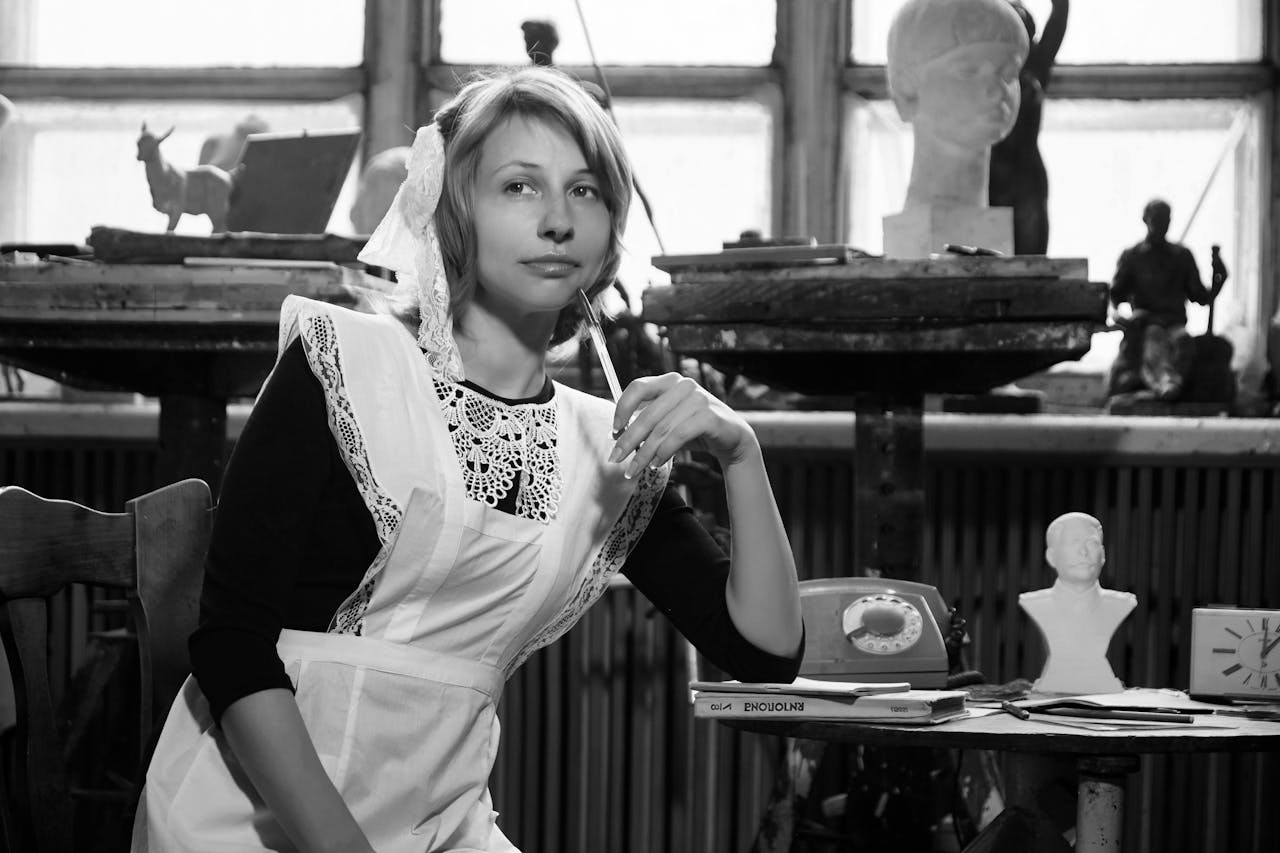 why-choose-us Black and white of young dreamy female in Soviet school uniform sitting on chair near table with retro telephone and books and looking away thoughtfully