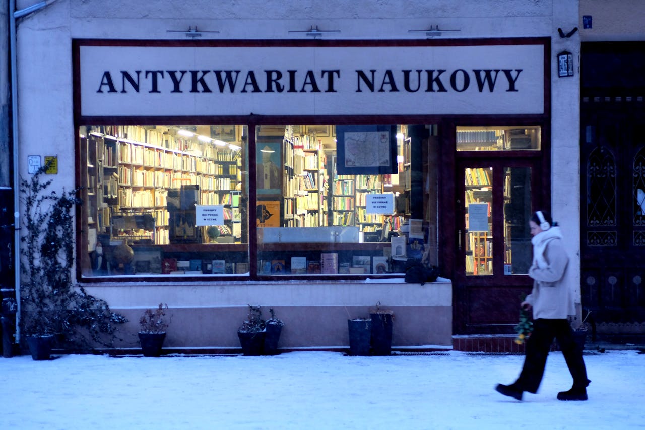 A person walks by a vintage bookstore named Antykwariat Naukowy in a snowy European street.
